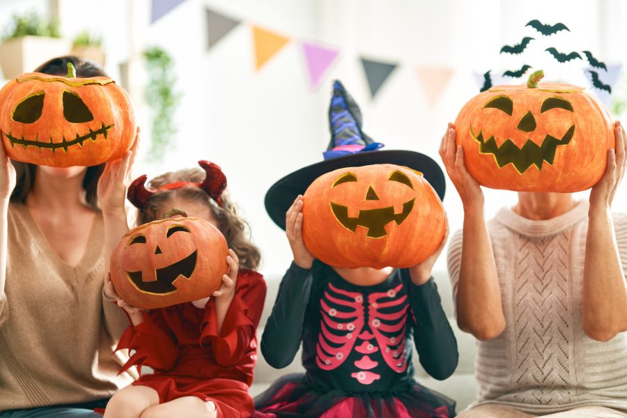 four children in halloween costumes holding pumpkins to their face