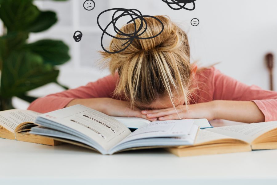 school aged child resting her head on school work with symbols around her head to indicate she may be stressed